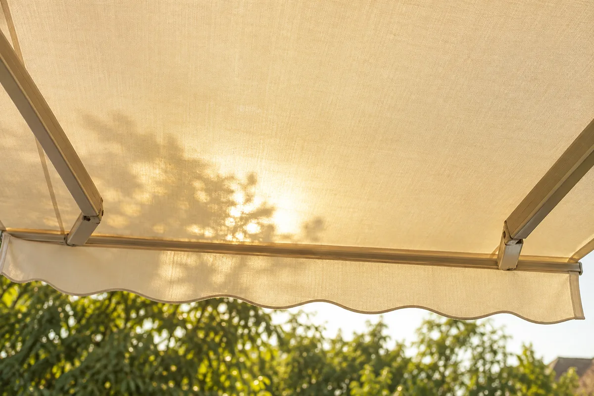 Toile de store banne écrue vue de dessous, traversée par une lumière douce